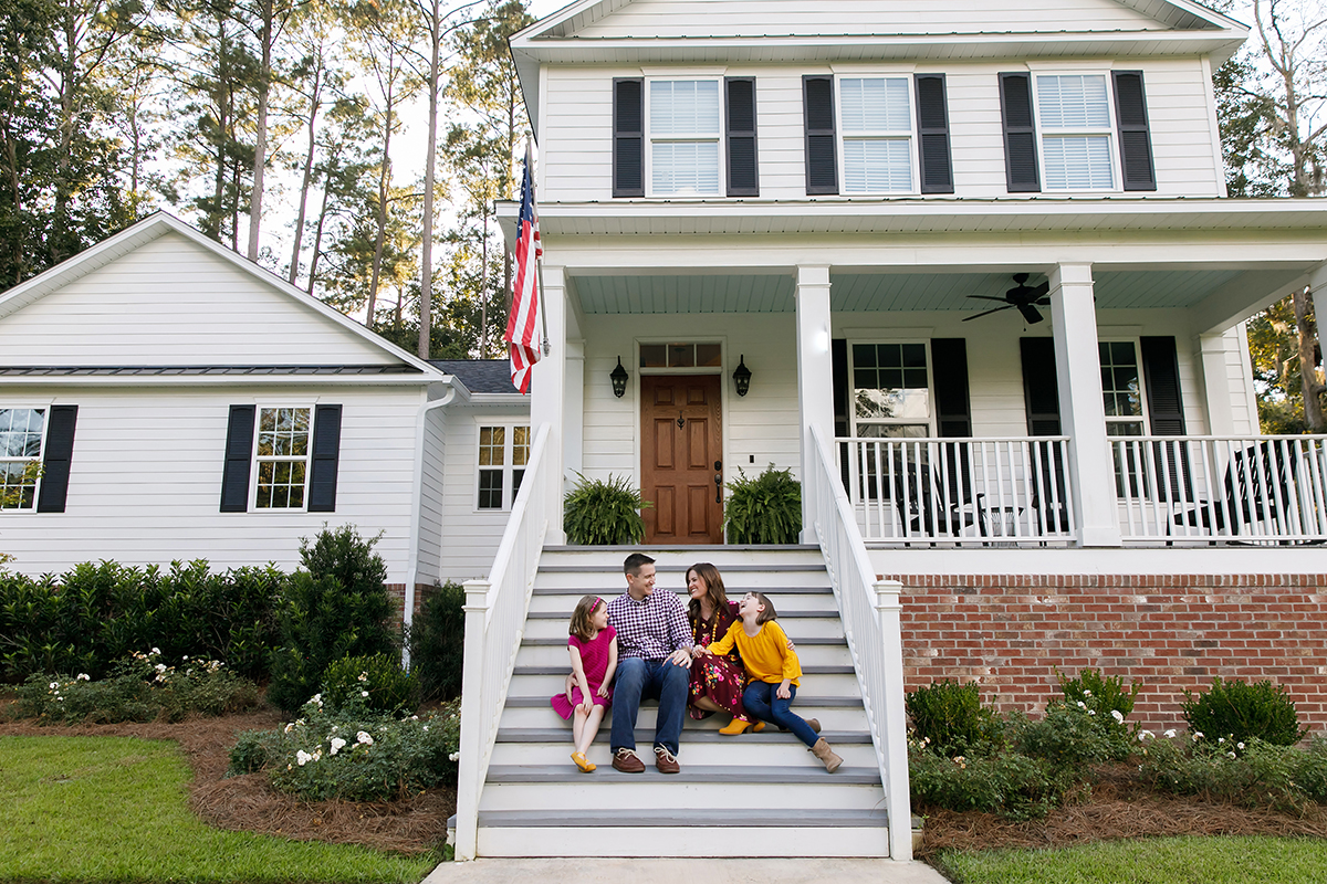 Family sitting outside on the steps of a new construction white siding farmhouse